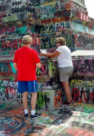 Woman reading from a Bible at the base of Robert E. Lee’s statue. Her mask is printed with the American flag
